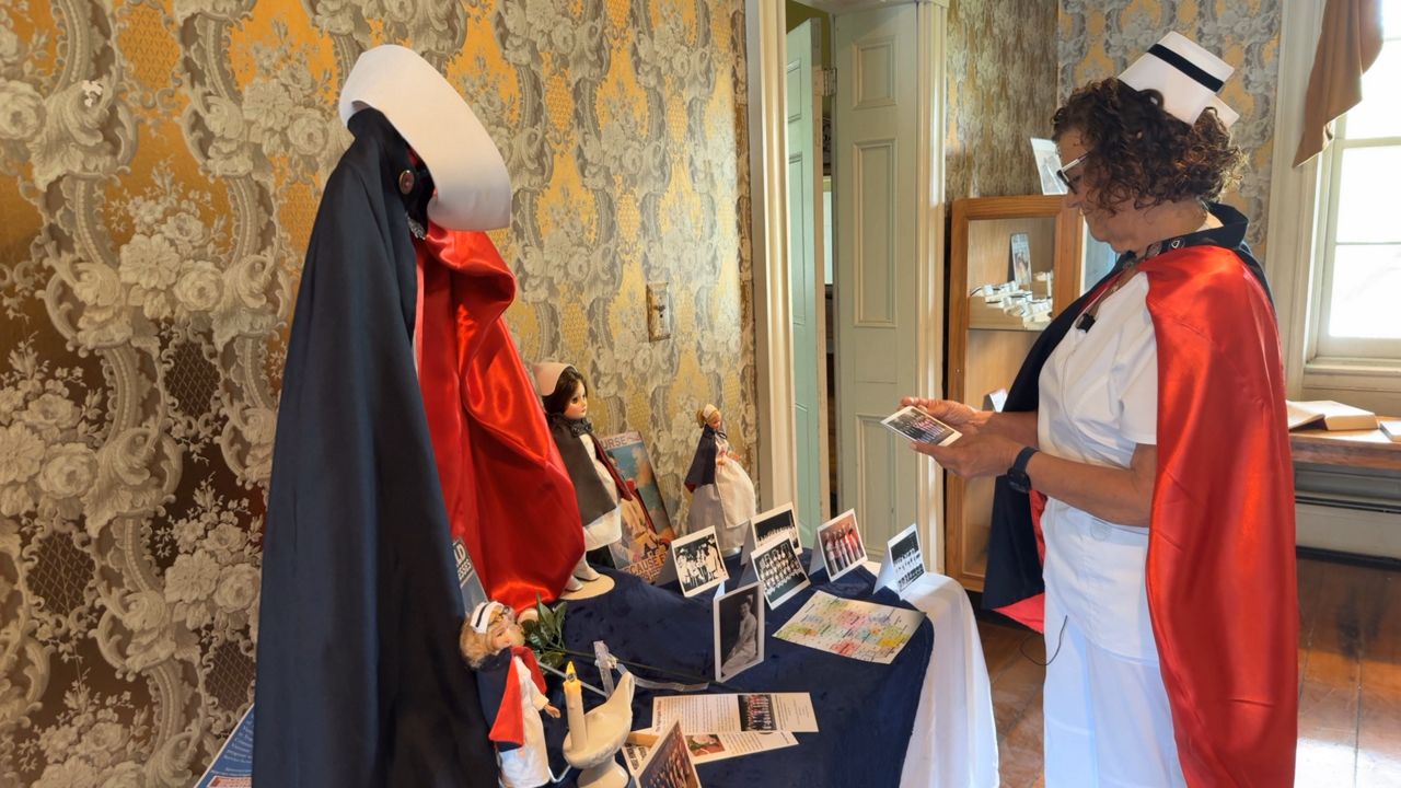 Lorie Prokup is the president and co-founder of the Nurse Honor Guard of Eastern Ohio and she stands next to a Nurse Honor Guard display in the Warren Heritage Center in Warren, Ohio. 