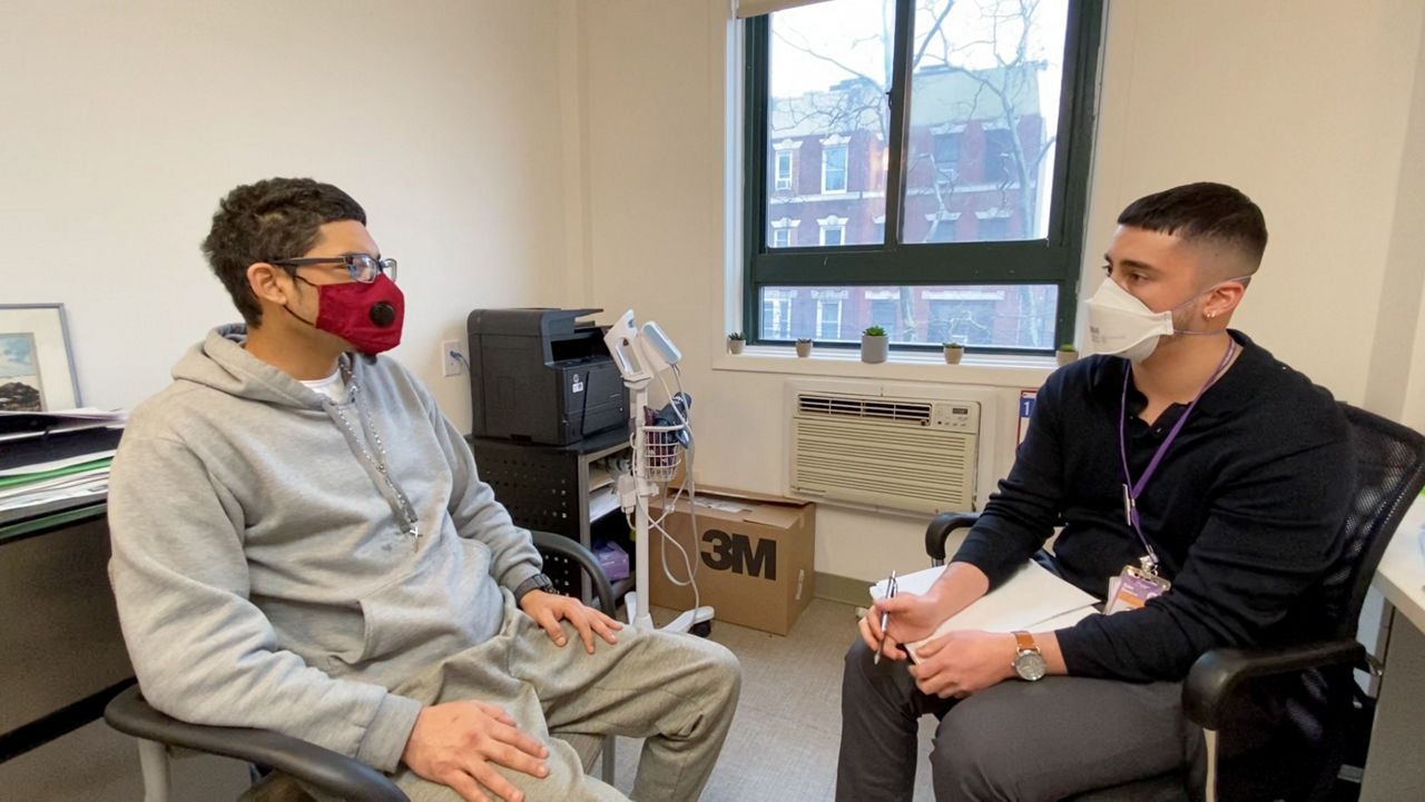 A nursing student sits across from a resident of a recovery center inside an office room, both men are wearing masks.