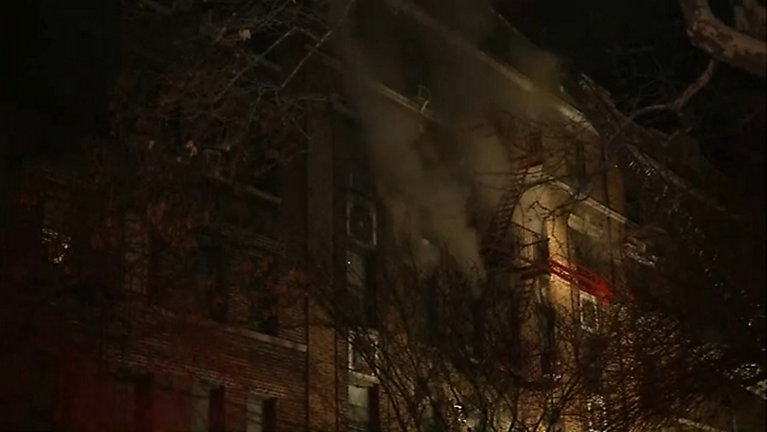 Dark smoke billows near a fire escape attached to a building.