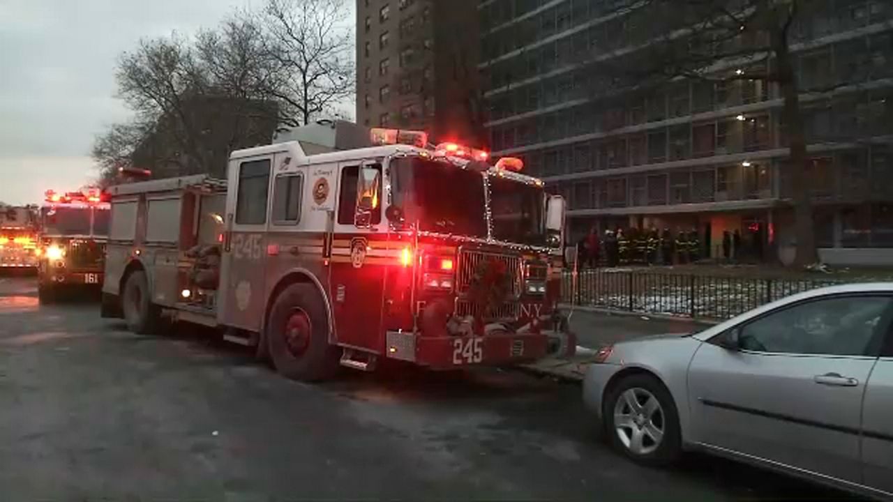 An FDNY truck parked on a street, with its lights on and a building in the background.