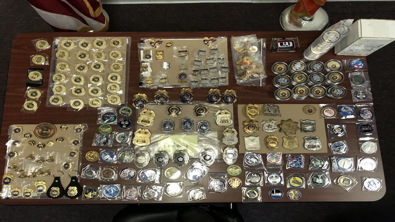 A bevy of metal police badges and memorabilia on a brown table. Some items are in clear plastic bags, while some rest on cardboard sheets.