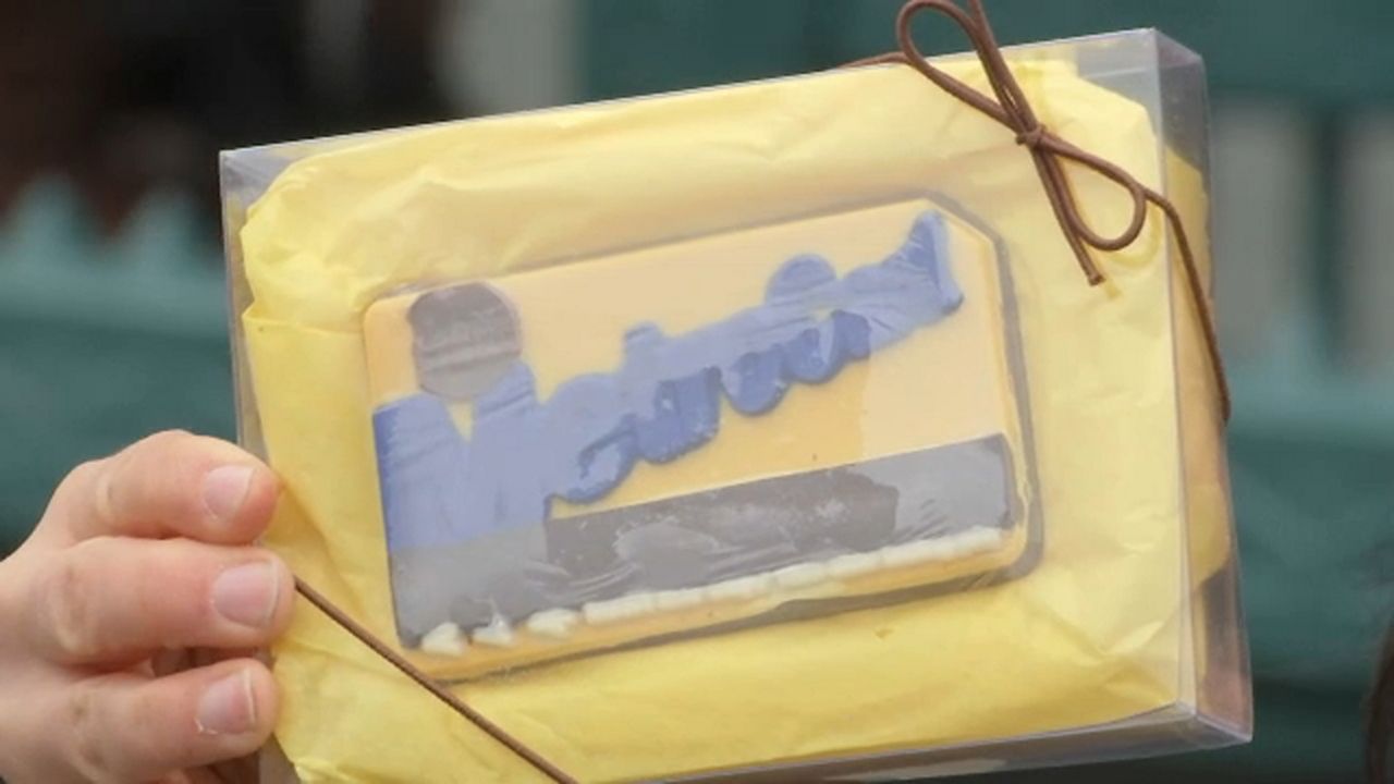 An MTA MetroCard replica sits in a yellow case inside a clear wrapper. A brown lace is tied around the top-right corner of the wrapper.