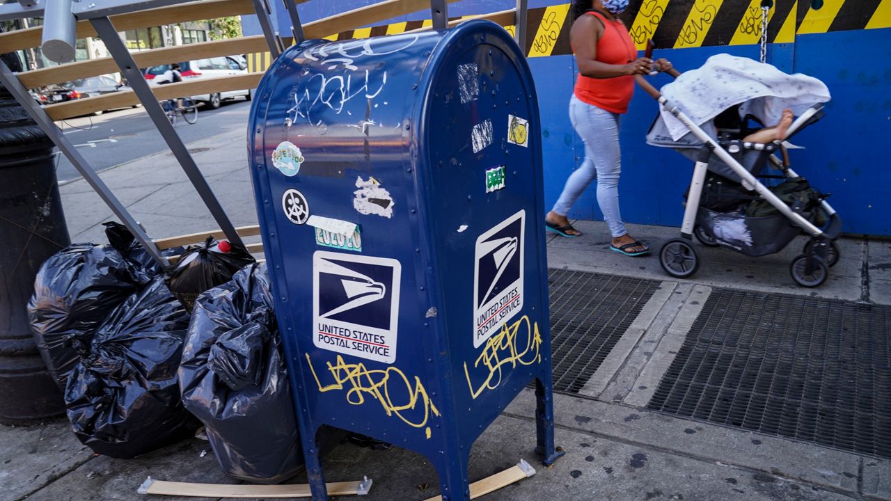 Pedestrians pass a USPS mailbox standing beside a pile of garbage on Fulton Street in the Brooklyn borough of New York, Monday, Aug. 17, 2020. (AP Photo/John Minchillo)
