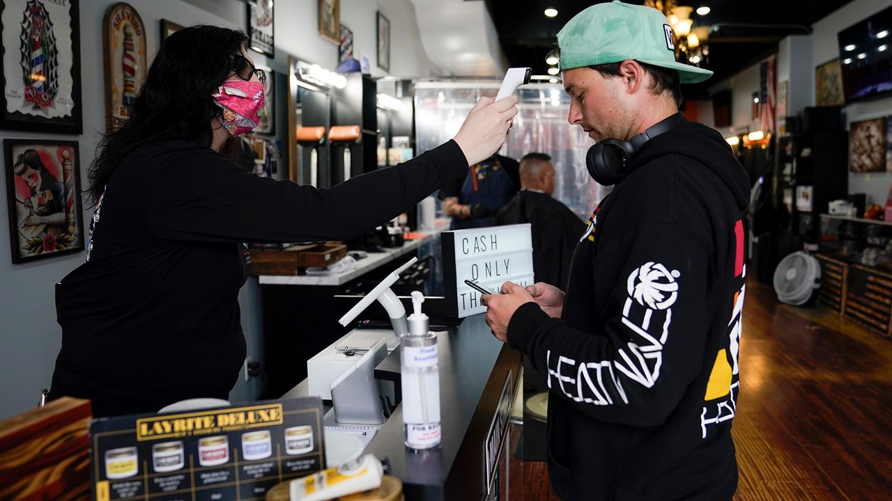 Josh Straight has his temperature taken by Melissa Acosta before getting his hair cut at Orange County Barbers Parlor during the coronavirus pandemic on Wednesday, May 27, 2020, in Huntington Beach, Calif. (AP Photo/Ashley Landis)