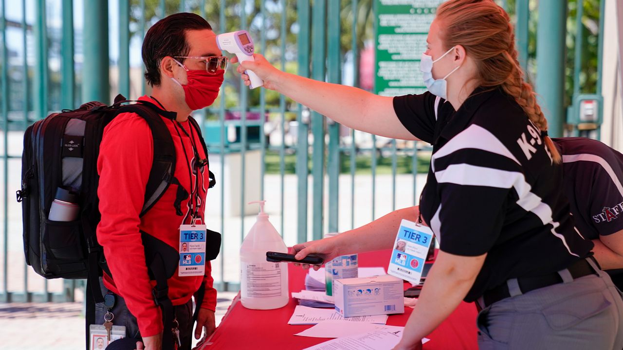 Ricardo Zapata, left, a photographer for the Los Angeles Angels, has his temperature taken by Sarah Morris before entering Angels Stadium for baseball practice on Monday, July 6, 2020, in Anaheim, Calif. New protocols like temperature checks, social distancing, and limiting amount of people allowed in sports venues have been put in place due to the spread of COVID-19. (AP Photo/Ashley Landis)