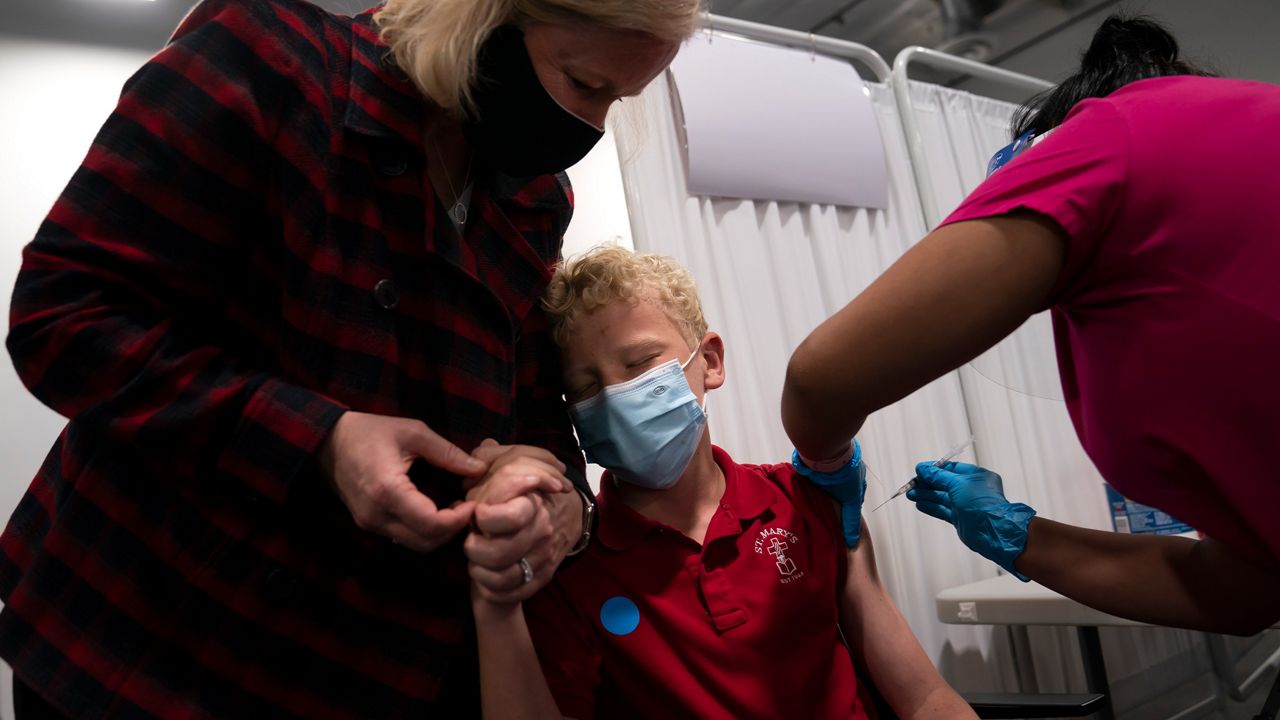 Heather Haworth, left, holds the hand of her 12-year-old son Jeremy as he receives the first dose of the Pfizer COVID-19 vaccine from medical assistant Gloria Urgell at Providence Edwards Lifesciences vaccination site in Santa Ana, Calif., Thursday, May 13, 2021. (AP Photo/Jae C. Hong)