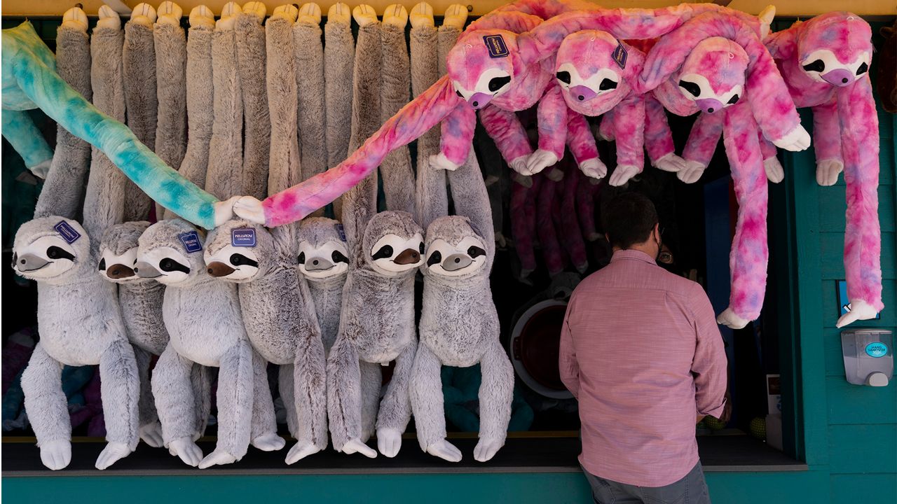 A man stands next to stuffed sloths during the Knott's Taste of Boysenberry Festival at Knott's Berry Farm in Buena Park, Calif., Tuesday, March 30, 2021. (AP Photo/Jae C. Hong)