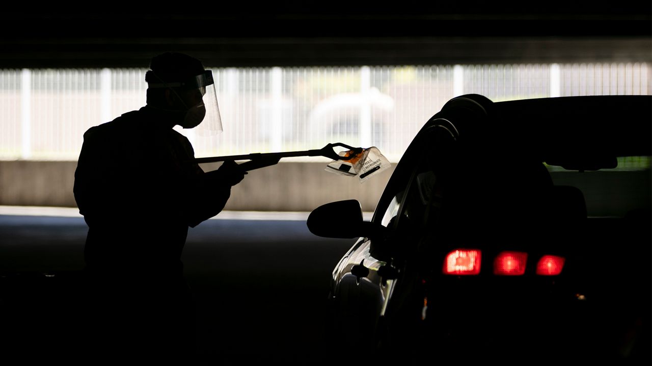 Physician assistant Calvin Tran uses a grabber to collect a nasal swab sample at a COVID-19 drive-through testing site set up at the Anaheim Convention Center in Anaheim, Calif., Thursday, July 16, 2020. Rising coronavirus infections across dozens of states are threatening the U.S. economic recovery, forcing businesses and consumers to freeze spending and keeping the unemployment rate stubbornly high. (AP Photo/Jae C. Hong)