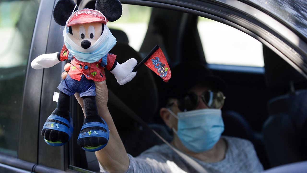 A Disney employee carries a Mickey Mouse doll during a drive-by protest to demand a safe reopening amid the coronavirus pandemic Saturday, June 27, 2020, in Anaheim, Calif. Workers are demanding regular testing, stricter cleaning protocols and higher staffing levels. Disney had originally proposed reopening on July 17th but announced this week it was postponing. (AP Photo/Marcio Jose Sanchez)