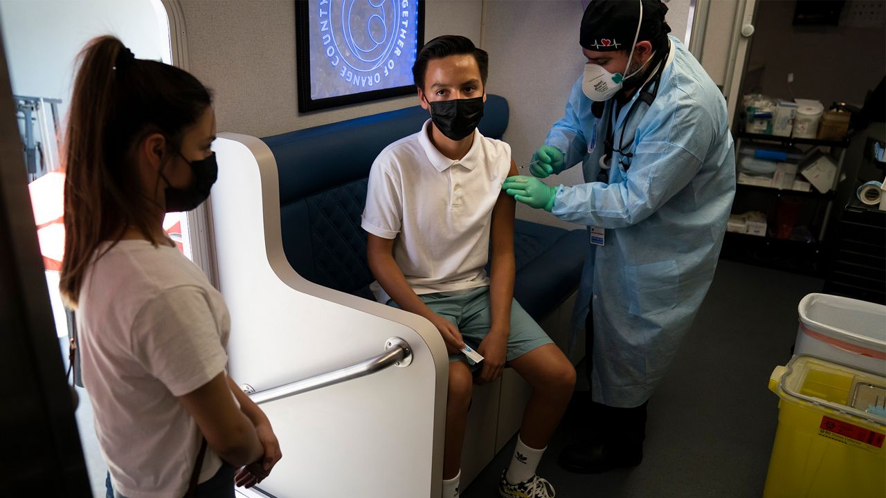 Rosie Manzo, left, watches as her brother, Esteban, 15, receives the Pfizer COVID-19 vaccine from Parsia Jahanbani in a mobile vaccine clinic operated by Families Together of Orange County Thursday, Aug. 26, 2021, in Santa Ana, Calif. (AP Photo/Jae C. Hong)