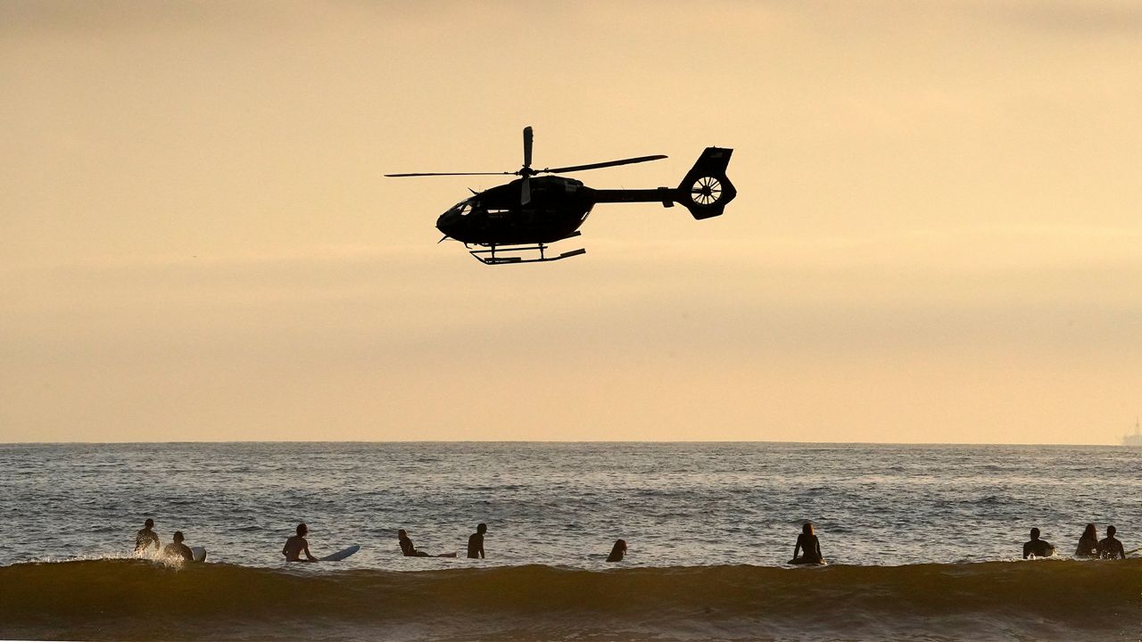 A helicopter flies over surfers the day before the beach is scheduled to close during the coronavirus outbreak, Thursday, April 30, 2020, in Newport Beach, Calif. California Gov. Gavin Newsom on Thursday temporarily closed Orange County's coastline after large crowds were seen there. (AP Photo/Mark J. Terrill)