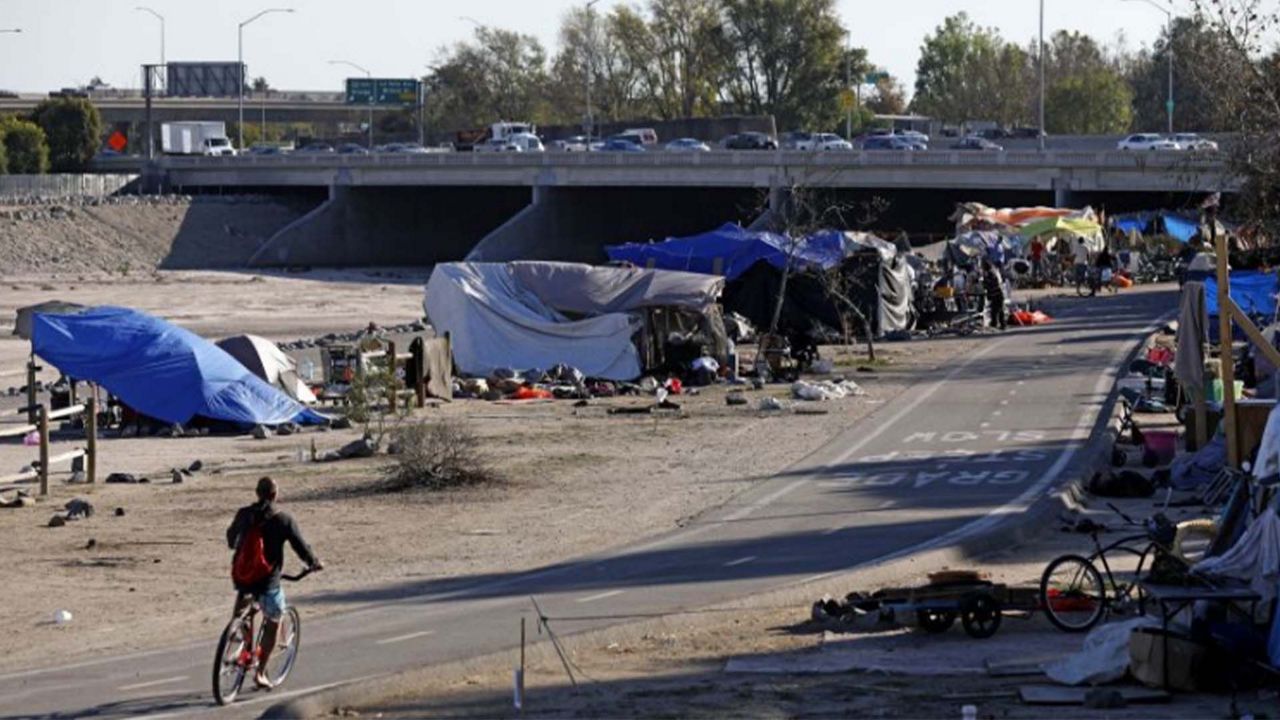 In this Sept. 14, 2017 file photo a cyclist passes the row of tents and tarps along the Santa Ana riverbed near Angel Stadium in Anaheim, Calif. (AP Photo/Jae C. Hong, File)