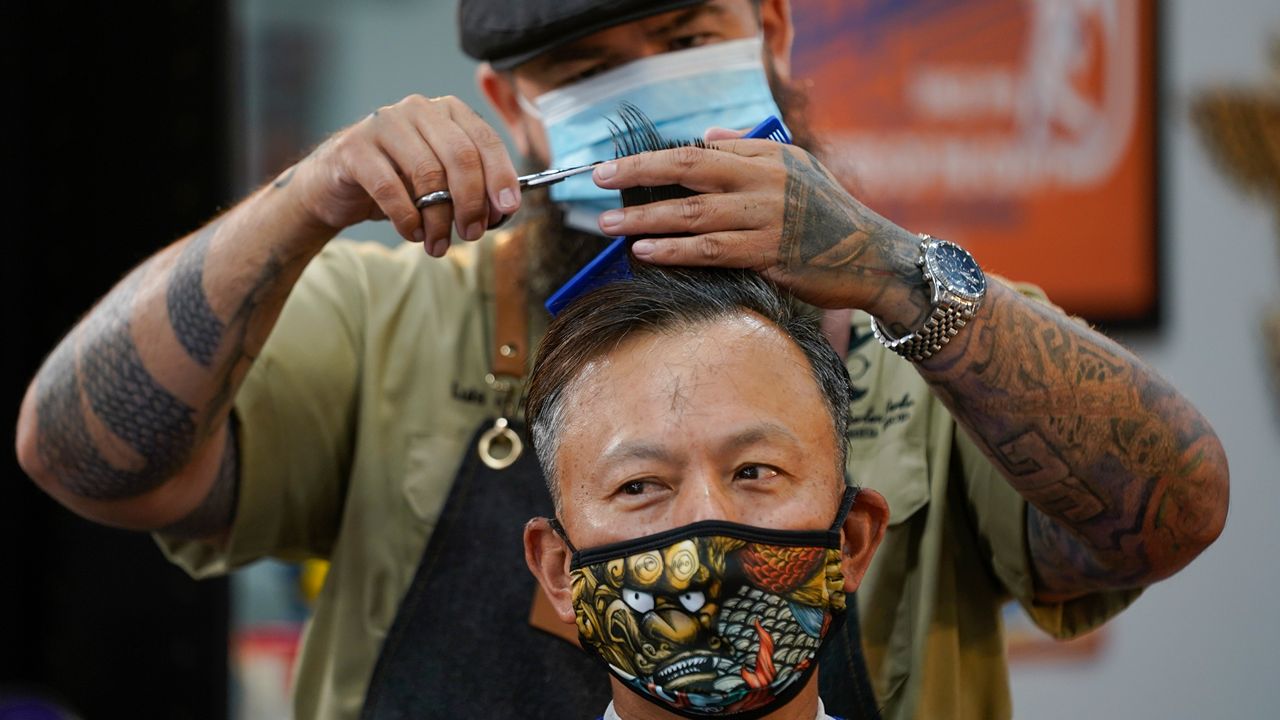 Luis Lopez wears a face mask while giving a hair cut to Alexander Chin at Orange County Barbers Parlor on Wednesday, May 27, 2020, in Huntington Beach, Calif. Orange County Barber shops and salons were allowed to open today. (AP Photo/Ashley Landis)