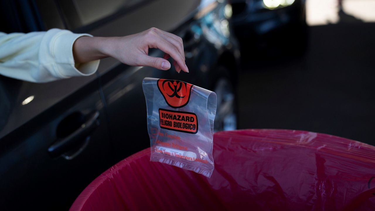 In this Nov. 16, 2020, file photo, a woman drops her nasal swab sample into a bin at a COVID-19 testing site set up at the OC Fairgrounds in Costa Mesa. (AP Photo/Jae C. Hong)