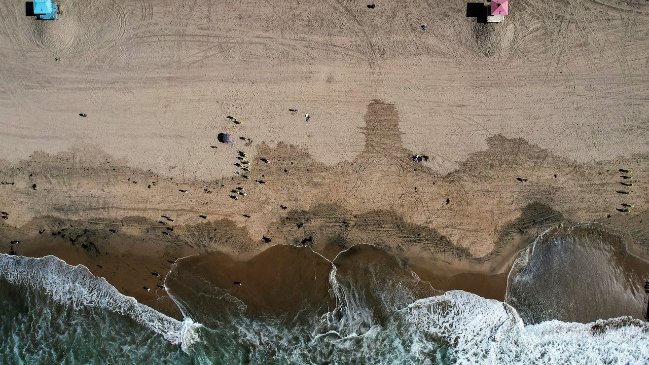 This aerial photo taken with a drone, shows beachgoers as workers in protective suits continue to clean the contaminated beach in Huntington Beach, Calif., on Oct. 11, 2021. (AP Photo/Ringo H.W. Chiu, File)