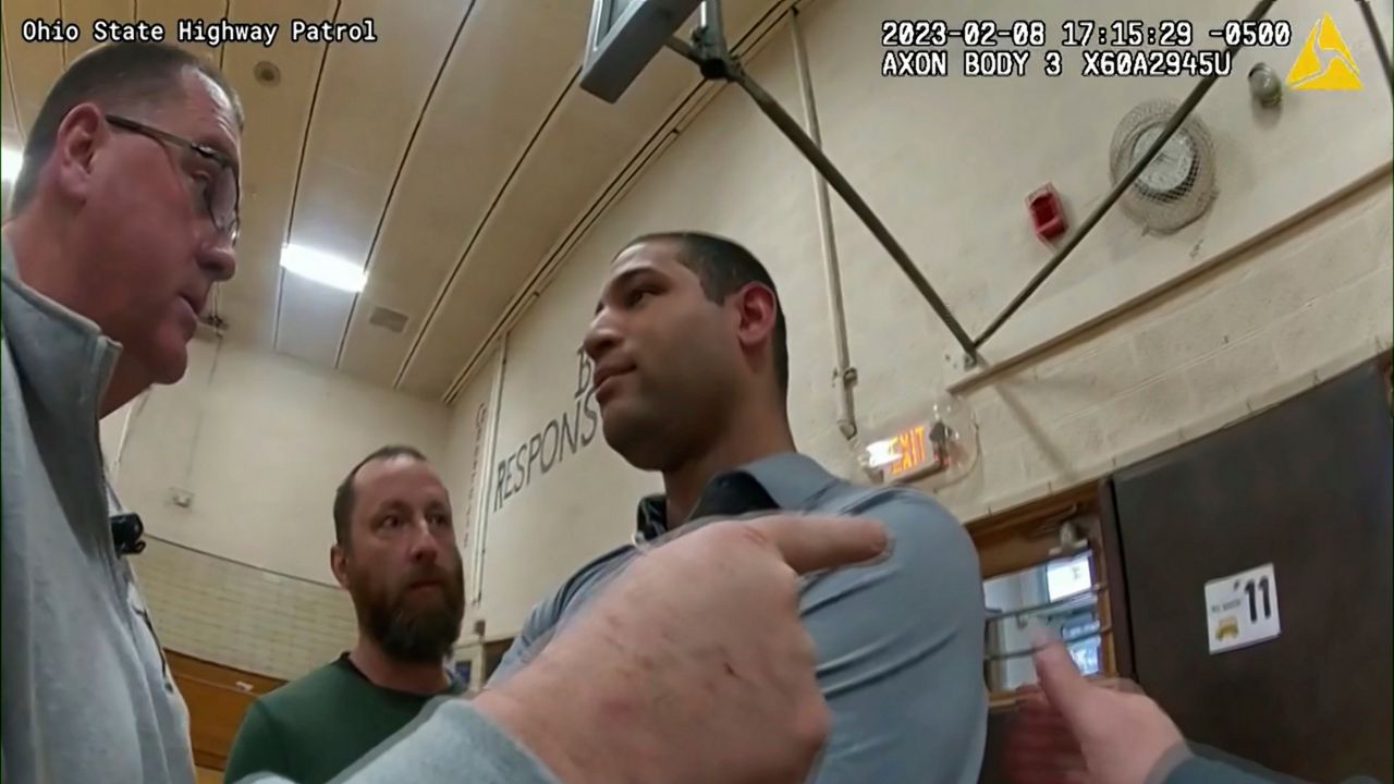 This photo provided by Ohio State Highway Patrol shows police bodycam footage of NewsNation correspondent Evan Lambert interaction with authorities Wednesday, Feb. 8, 2023 in the gymnasium of an elementary school in East Palestine, Ohio. Lambert was charged with criminal trespass and resisting arrest after authorities said he was told to stop his live broadcast and then refused their orders to leave the news conference with Ohio Gov. Mike DeWine. (Ohio State Highway Patrol via AP)