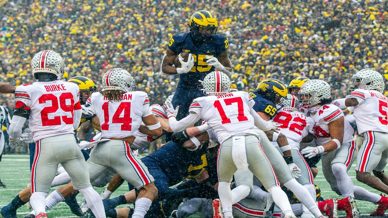 Michigan running back Hassan Haskins (25) leaps over Ohio State defenders for a touchdown in the second quarter of an NCAA college football game in Ann Arbor, Mich., Saturday, Nov. 27, 2021. (AP Photo/Tony Ding)