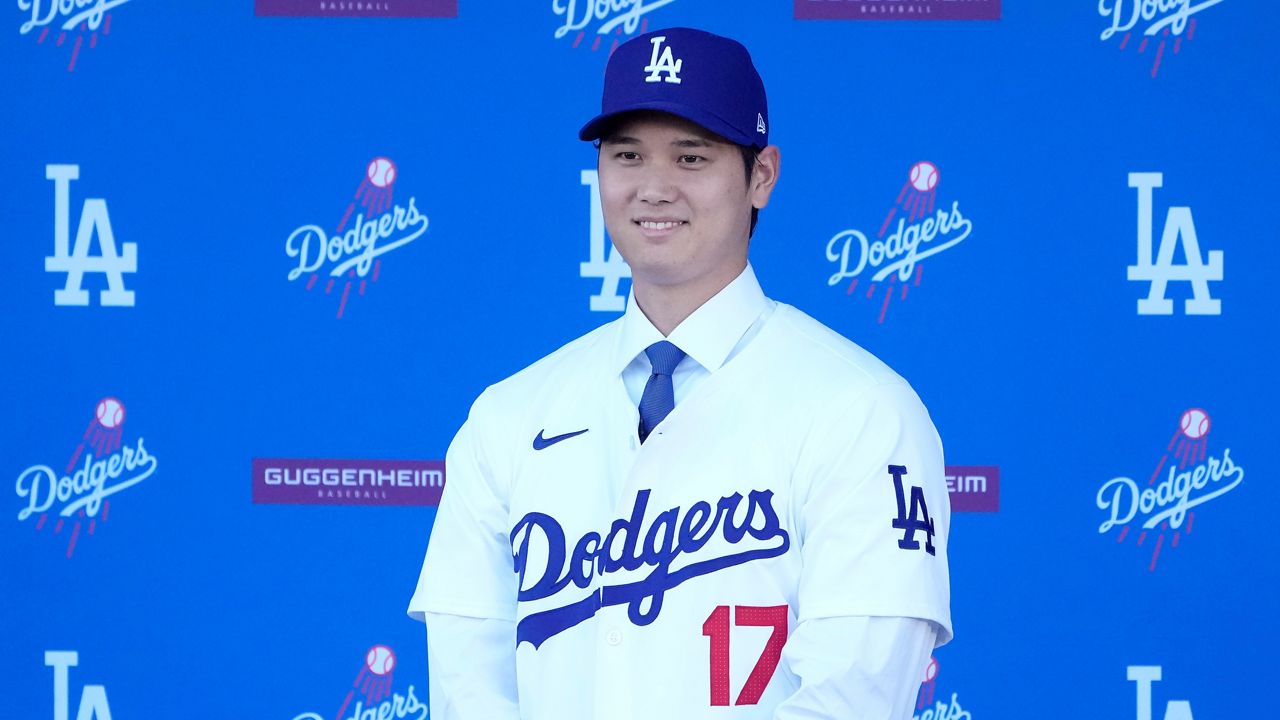 Los Angeles Dodgers' Shohei Ohtani smiles while wearing a jersey and baseball cap during a news conference at Dodger Stadium Thursday, Dec. 14, 2023, in Los Angeles. (AP Photo/Marcio Jose Sanchez)