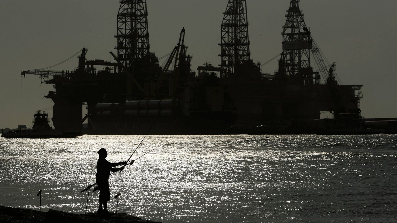 A man fishes near docked oil drilling platforms on May 8, 2020, in Port Aransas, Texas. (AP Photo/Eric Gay, File)