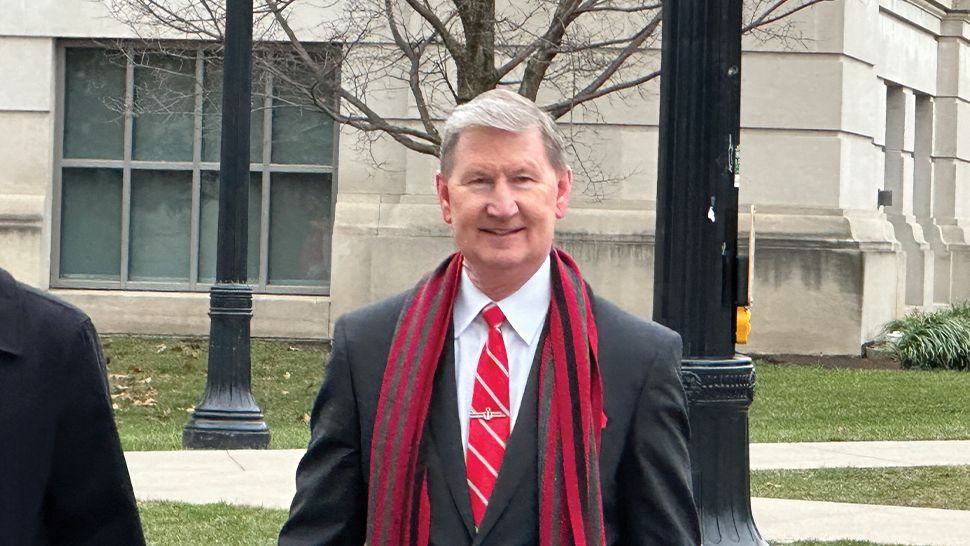 Walter "Ted" Carter, Jr., President, The Ohio State University wears a dark suit with a red tie and wool scarf as he walks across campus. 