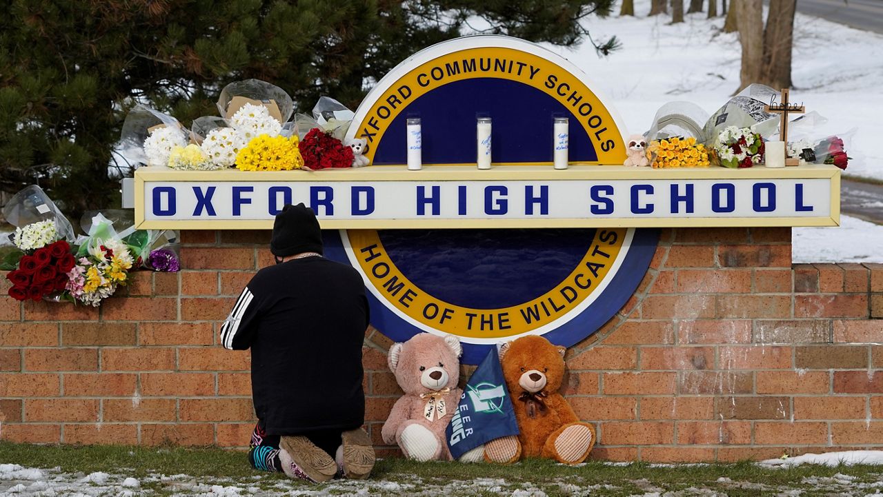 A well wisher kneels to pray at a memorial on the sign of Oxford High School in Oxford, Mich., Wednesday, Dec. 1, 2021. A 15-year-old sophomore opened fire at the school, killing several students and wounding multiple other people, including a teacher. (AP Photo/Paul Sancya)