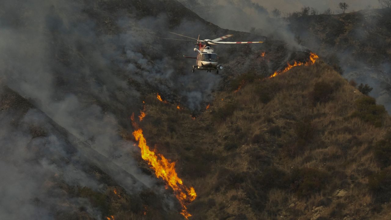 A firefighting helicopter flies away after dropping water over a brush fire scorching at least 100 acres in the Pacific Palisades area of Los Angeles Saturday, May 15, 2021. (AP Photo/Ringo H.W. Chiu)