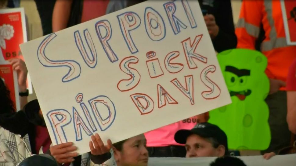 An advocate holds up a sign that says "Support Paid Sick Days" in this Spectrum News file photograph. (Spectrum News Images)