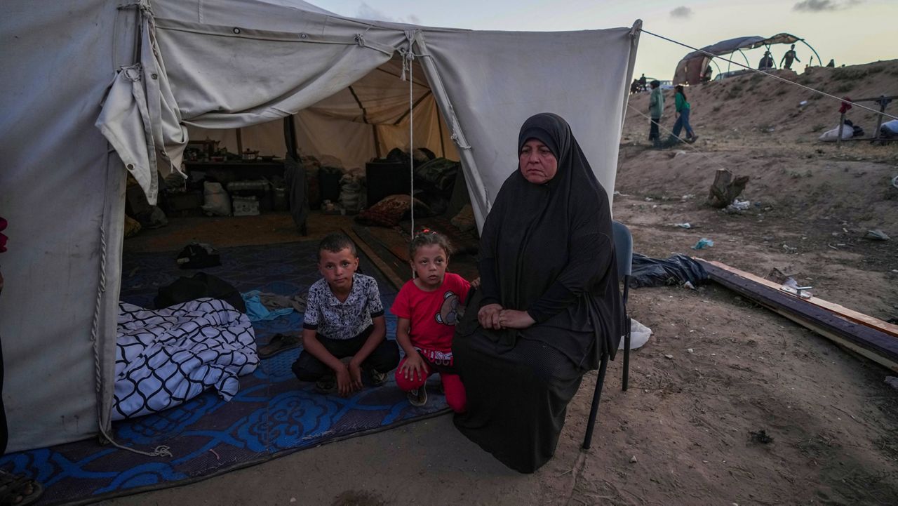 A Palestinian woman sits in front of her makeshift tent with her grandchildren after been displaced by the Israeli air and ground offensive on the Gaza Strip at a camp in Deir al Balah, Monday, May 13, 2024. (AP Photo/Abdel Kareem Hana)