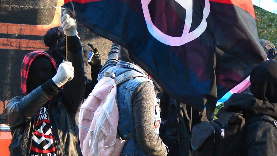 Rose City Antifa activists with modified Red and black flag and Transgender flags in a protest against Patriot Prayer in 2017. (By Old White Truck from USA - Patriot Prayer vs Antifa protests. Photo 11 of 14, CC BY-SA 2.0, https://commons.wikimedia.org/w/index.php?curid=64734850). This image was cropped in order to display in a 16x9 format. 
