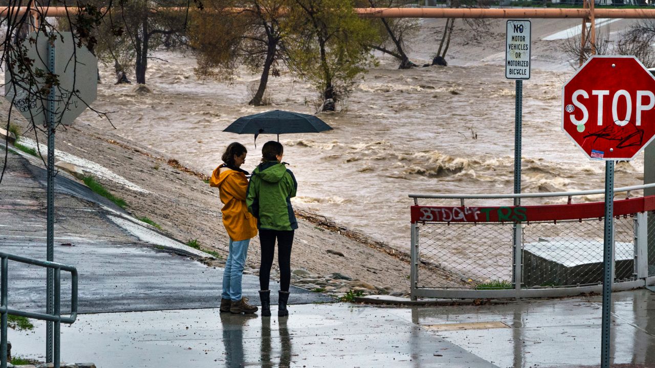 People watch the high volume of storm rain water flowing downstream at the Los Angeles River in Los Angeles on Saturday, Jan. 14, 2023. (AP Photo/Damian Dovarganes)