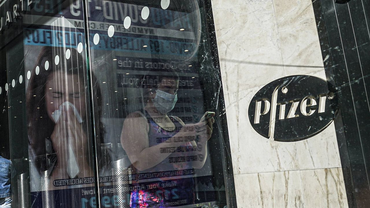 An ad for COVID-19 testing reflects on glass at a bus stop, as pedestrians walk past Pfizer world headquarters in New York. (AP Photo/Bebeto Matthews, File)