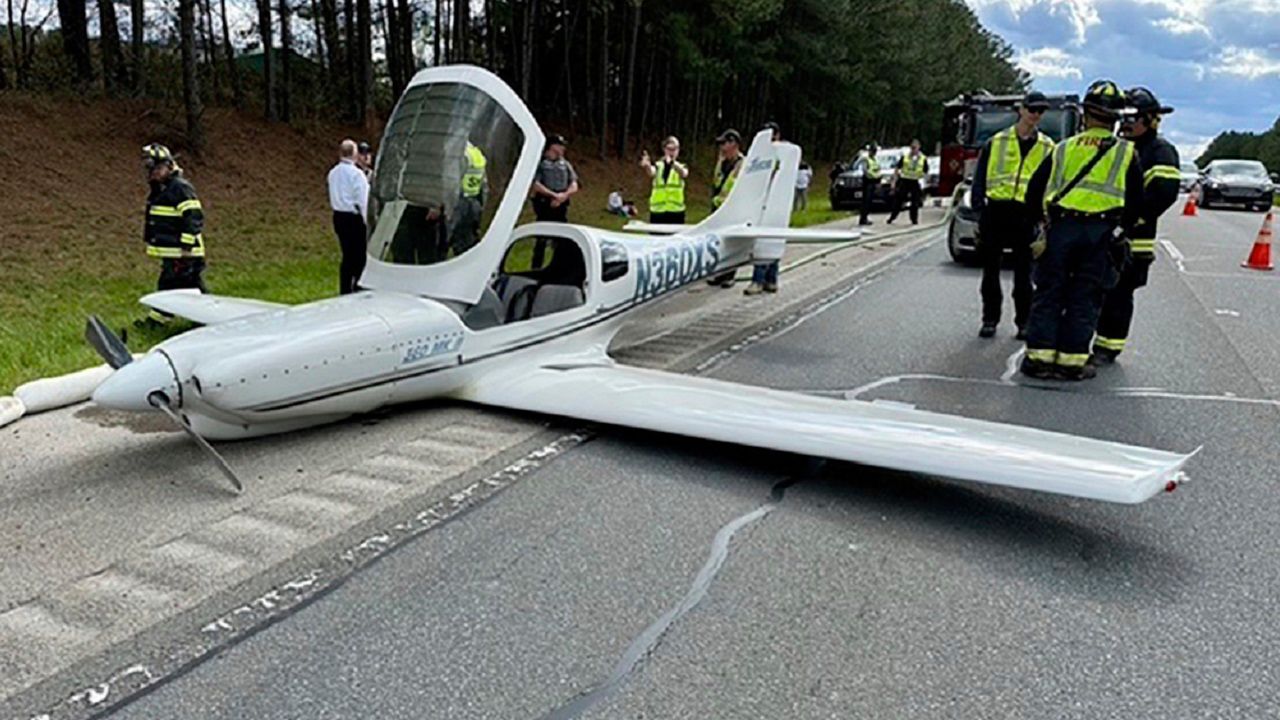 In this image provided by the Moncure, N.C., Fire Department, emergency personnel and law enforcement look over the scene after a small plane, experiencing engine problems, made an emergency landing along Route 1, Thursday afternoon, April 4, 2024, in Moncure, N.C., near Raleigh Executive Jetport at Sanford-Lee County Airport. The plane struck two vehicles as it landed, but no injuries were reported, authorities said. (Moncure Fire Department via AP)