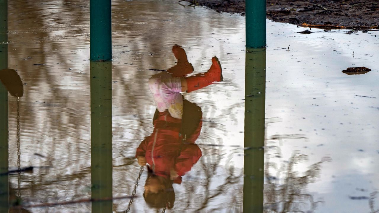 A young girl swings over a flooded playground at Covered Bridge County Park in Felton, Calif., Tuesday, Jan. 10, 2023. (AP Photo/Nic Coury)