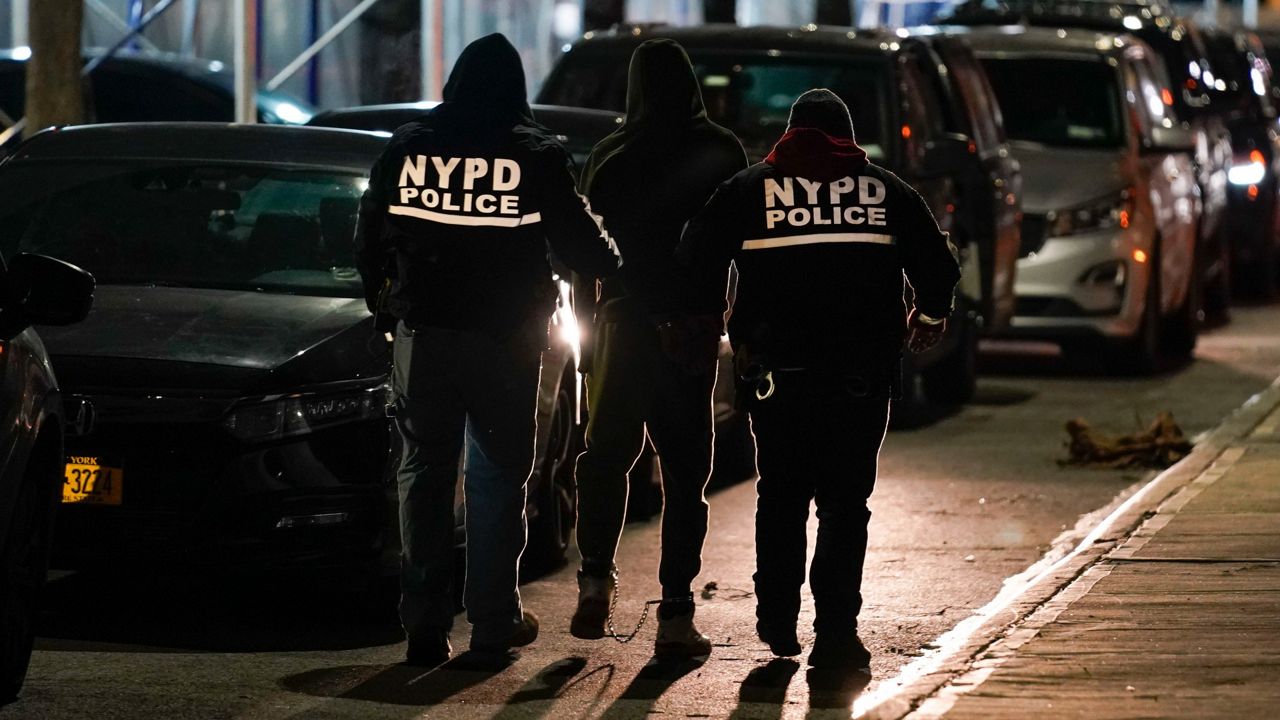 Police officers escort a handcuffed suspect to a car during a raid in Brooklyn, Jan. 4, 2022.  Law enforcement officials have credited similar raids in the borough with declining shooting rates. (AP Photo/Seth Wenig)