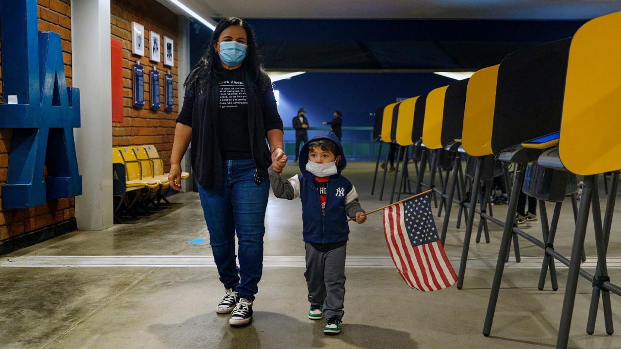 Lisa Carrera, a former Los Angeles Unified School history teacher from La Puente, Calif., holds the hand of her grandson Maverick, 2, after casting her ballot in-person at the Top of the Park at Dodger Stadium in Los Angeles, Monday, Nov. 2, 2020. (AP Photo/Damian Dovarganes)