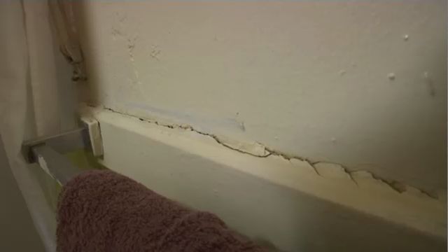 A wall behind a towel. A large crack is visible at the base of the wall.