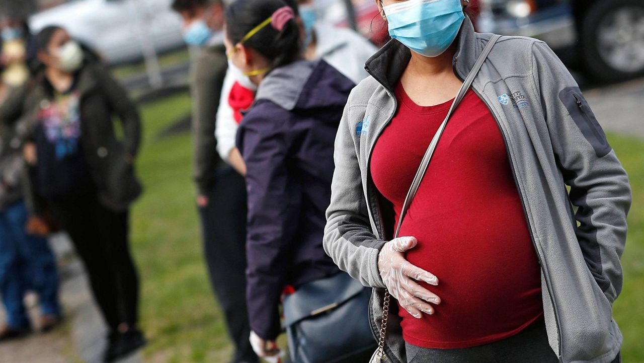 A pregnant woman wearing a face mask waits in line for groceries at a food pantry in Waltham, Mass. (AP Photo/Charles Krupa, File)