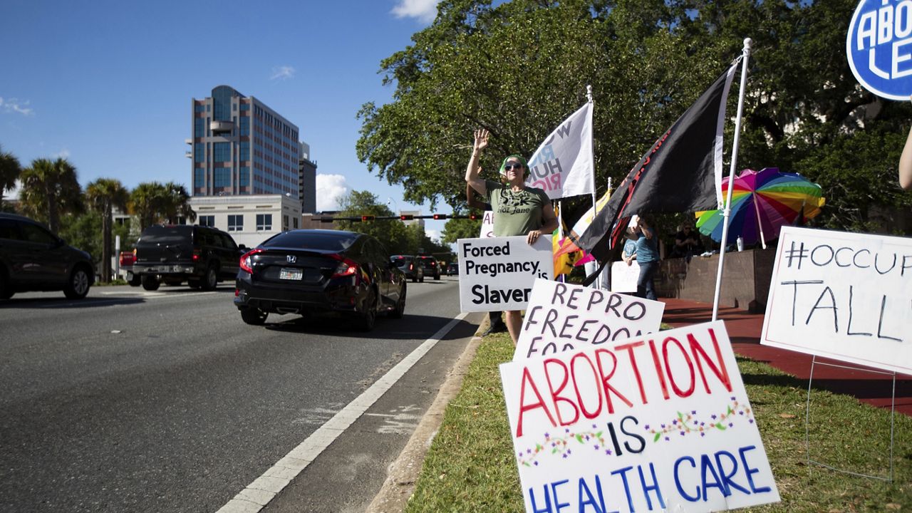 A small crowd holding signs and waving as cars pass by the Leon County Courthouse, protests Sb 300, which bans abortions after six weeks, Thursday, April 13, 2023. in Tallahassee, Fla. (Alicia Devine/Tallahassee Democrat via AP)