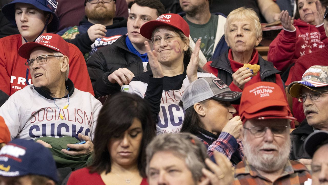 A member of the audience with a Q drawn on he cheek cheers before the start of a campaign rally for President Donald Trump, Monday, Feb. 10, 2020, in Manchester, N.H. 