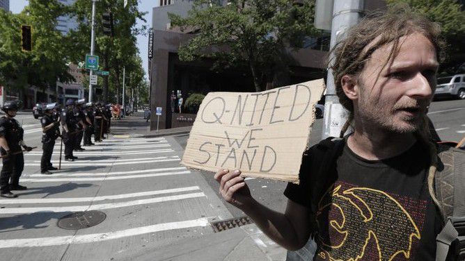 In this Aug. 18, 2018 file photo man holds a sign that reads "Q-Nited We Stand" during a rally held by members of Patriot Prayer and other groups supporting gun rights near City Hall in Seattle. (AP Photo/Ted S. Warren, file)