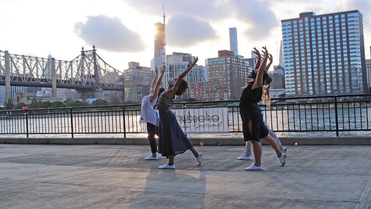 A group of dancers with arms outstretched mid-dance along the water in NYC. 