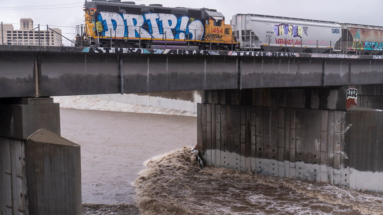 A cargo train passes over a bridge where a submerged vehicle is wedged against the bridge's pillar in the surging Los Angeles River making it difficult for firefighters to access it on Tuesday, Dec. 14, 2021 in Los Angeles. (AP Photo/Damian Dovarganes)