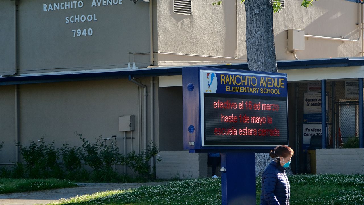 A woman wearing a protective mask to protect against coronavirus, walks her dog past the Ranchito Avenue Elementary School in the Panorama City section of Los Angeles on Wednesday, April 15, 2020. Classes on, then off again. These are just a few of the possible scenarios for California schools after Gov. Gavin Newsom laid out a roadmap for reopening the state amid the coronavirus outbreak.(AP Photo/Richard Vogel)