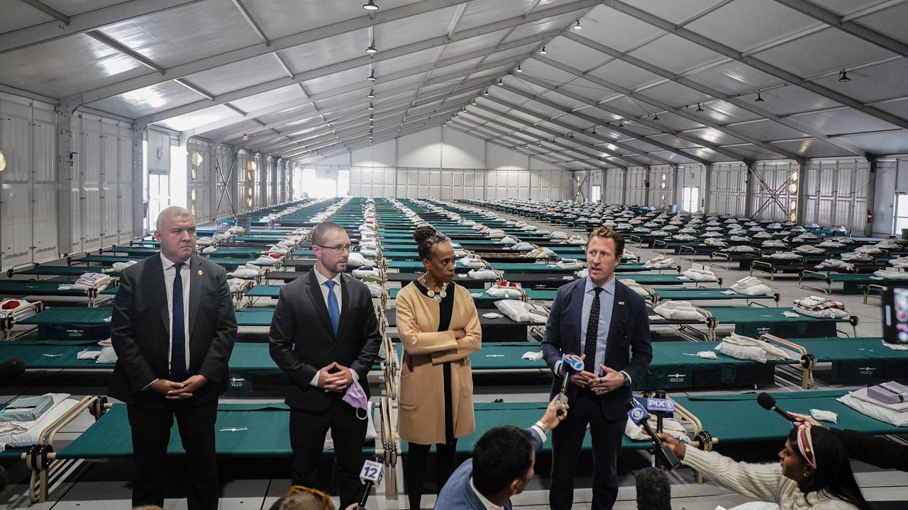 New York's Office of Immigrant Affairs Commissioner Manuel Castro, far left, Health and Hospital Vice President Dr. Ted Long, second from left, Deputy Mayor for Health and Human Services Anne Williams-Isom, second from right, and Emergency Management Commissioner Zach Iscol, far right, hold a news briefing in the sleeping area of the city's latest temporary shelter on Randall's Island, Oct. 18, 2022, in New York. (AP Photo/Bebeto Matthews)