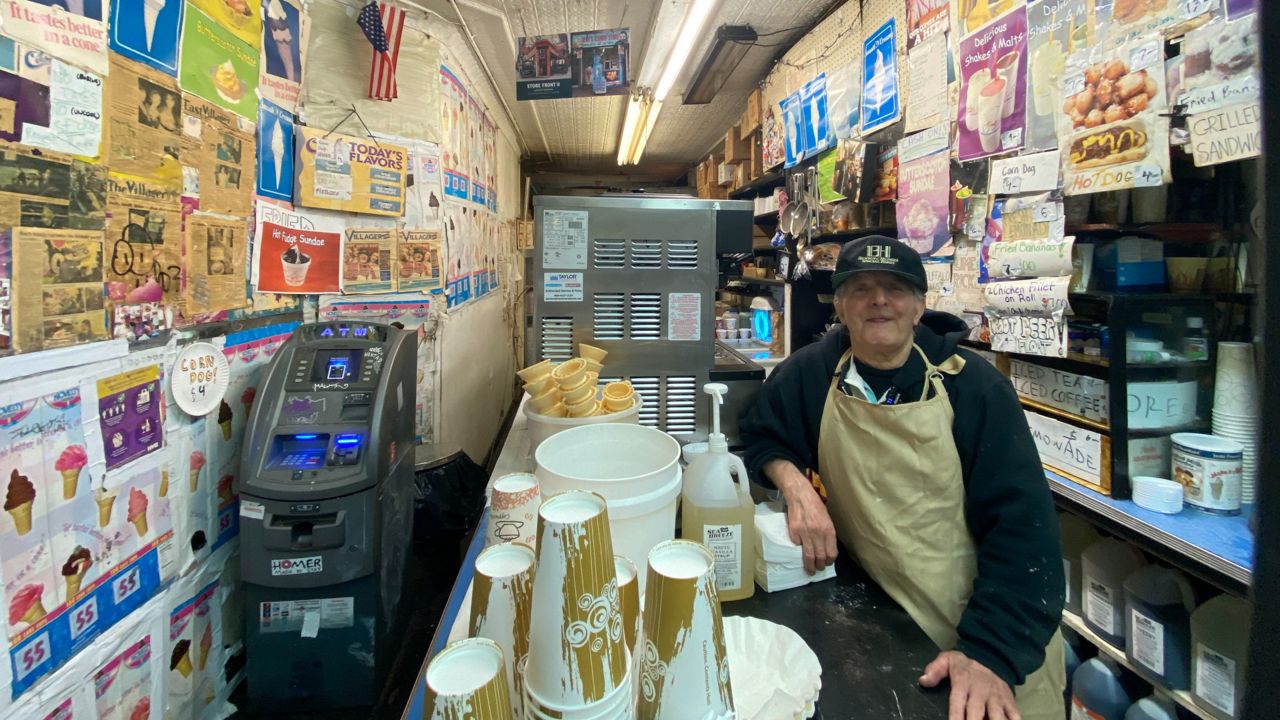 Ray stands behind the counter of his candy store, ATM on the other side of counter