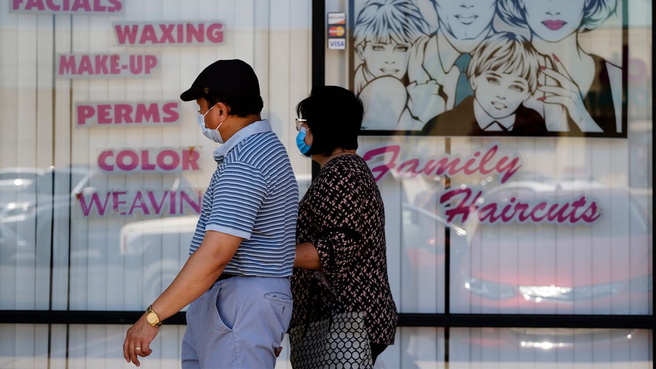 A couple wearing protective masks from coronavirus walk by a closed hair salon in the Panorama City section of Los Angeles on Tuesday, July 14, 2020. As the coronavirus swept California with renewed ferocity, the governor once again closed bars, inside dining and, for much of the state, gyms, indoor church services and hair and nail salons in an effort to prevent COVID-19 cases from swamping hospitals. (AP Photo/Richard Vogel)