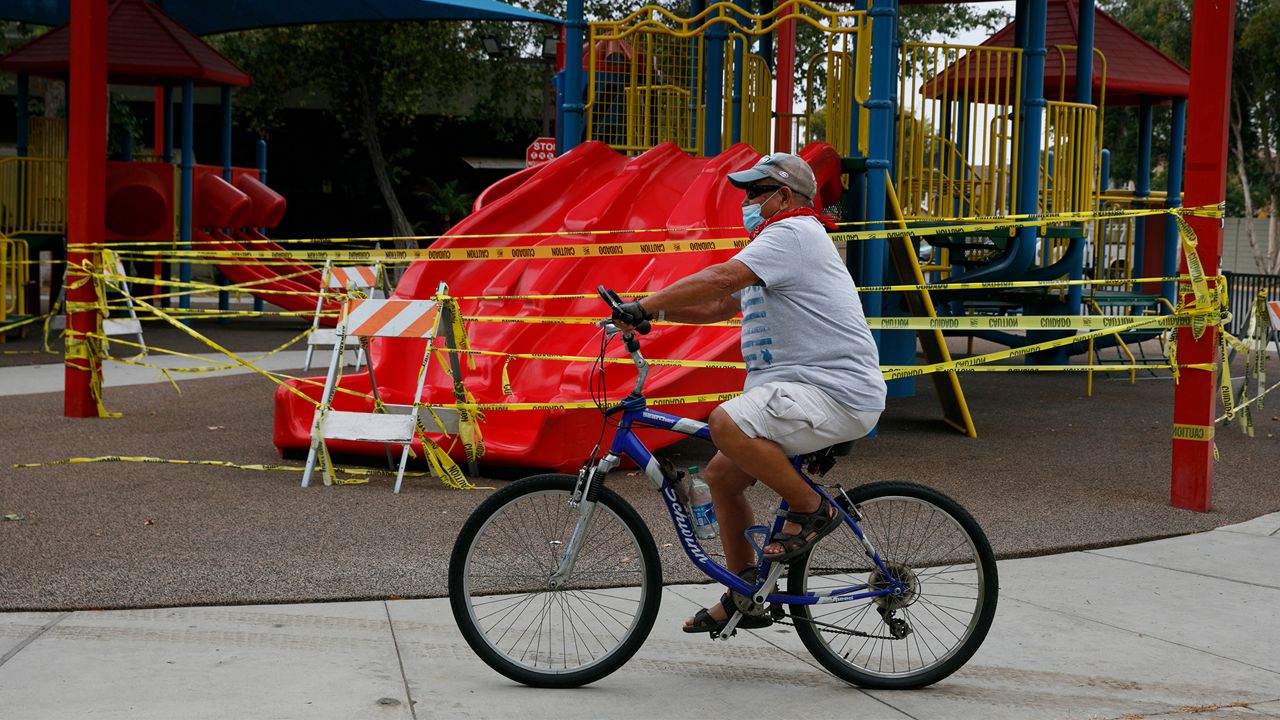 A man with a face mask rides his bicycle past a playground sealed off due to the coronavirus pandemic, Wednesday, July 1, 2020, in Commerce, Calif. California Gov. Gavin Newsom has ordered a three-week closure of bars and indoor operations of restaurants certain other businesses in Los Angeles and 18 other counties. (AP Photo/Jae C. Hong)