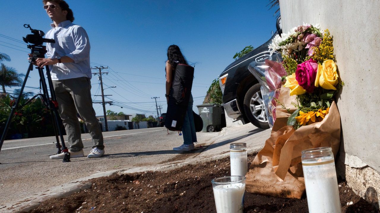 Reporters stand by a streetwise memorial of candles and flowers placed along Pacific Coast Highway, after a crash that killed four college students and injured two others, in Malibu, Calif., Oct. 19, 2023. (AP Photo/Richard Vogel)