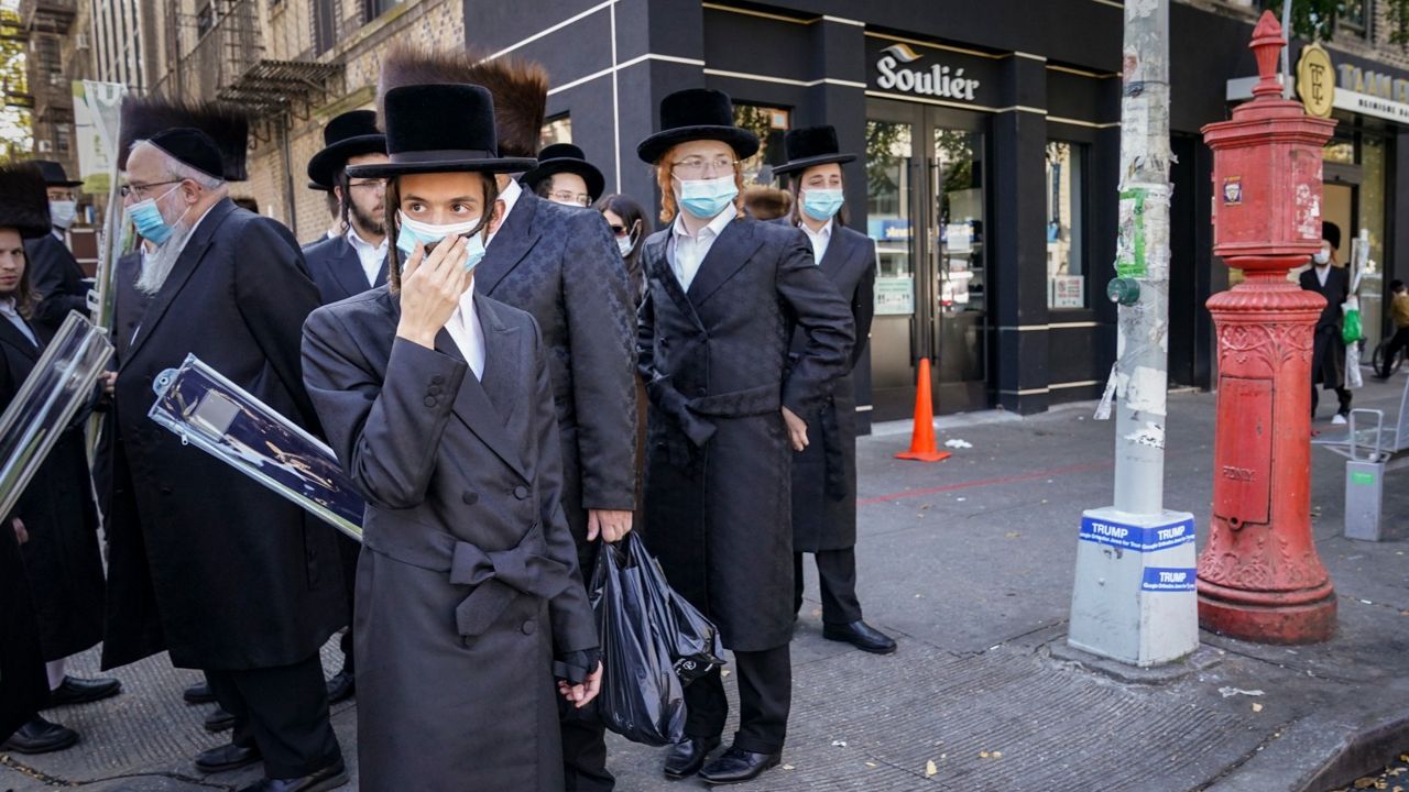 Members of Orthodox Jewish community stand at street corner with face masks on.