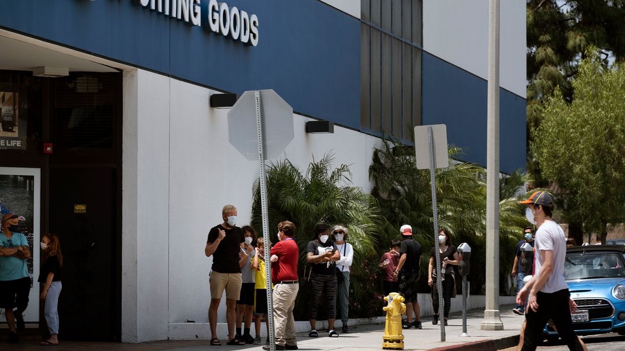 Shoppers line up wearing protective masks from the new coronavirus while waiting to enter a Big 5 Sporting Goods store in a popular shopping area in Santa Monica, Calif., on Saturday, May 9, 2020. Los Angeles County permitted the reopening of trails and golf courses but with social distancing restrictions. Weekend shoppers can visit bookstores, as well as stores for jewelry, toys, clothing, shoes, home supplies and furnishing, sporting goods, antiques and music. (AP Photo/Richard Vogel)
